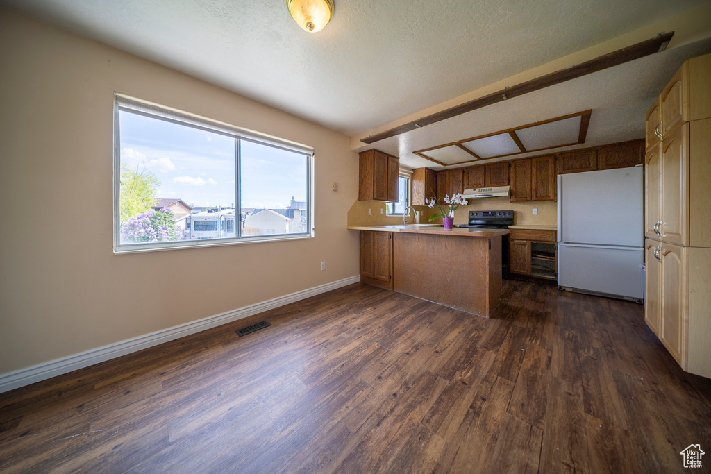 Kitchen featuring dark wood-style flooring, black electric range, freestanding refrigerator, a peninsula, and visible vents