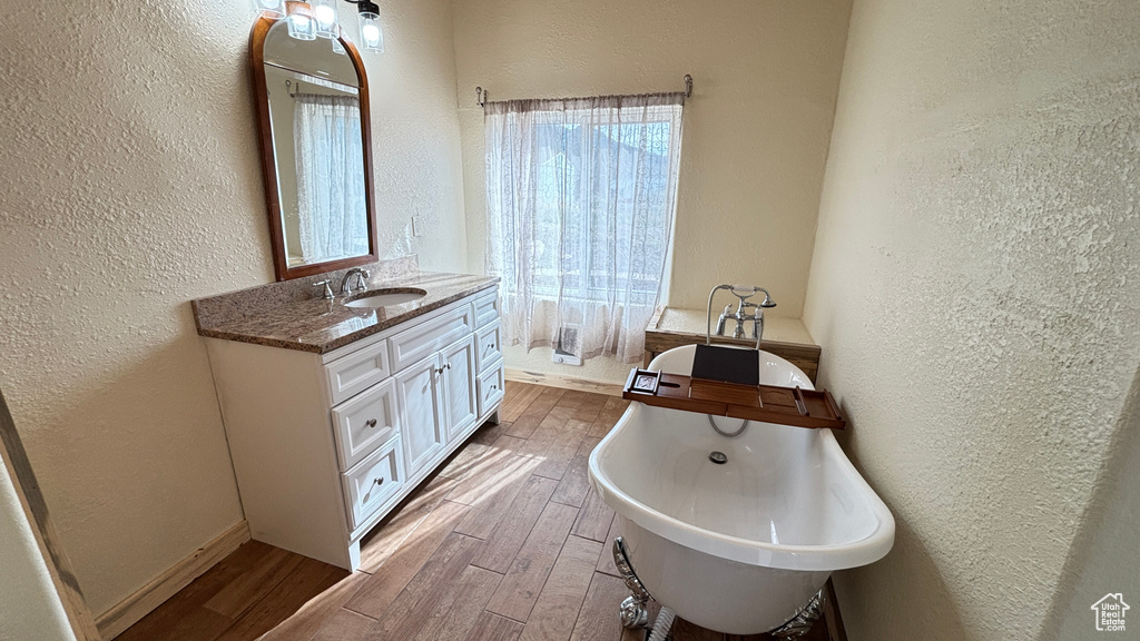 Full bathroom featuring a soaking tub, a textured wall, wood finished floors, and vanity