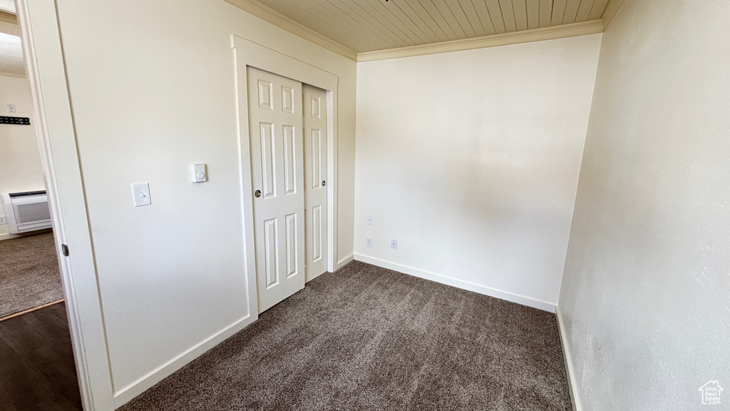 Unfurnished bedroom featuring a closet, crown molding, dark carpet, and baseboards