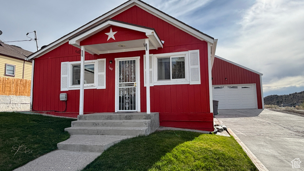 Bungalow-style home with fence, a front lawn, entry steps, and a detached garage