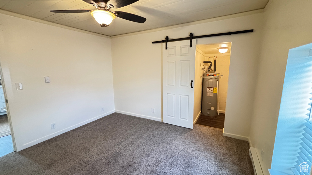 Unfurnished bedroom featuring baseboards, water heater, a barn door, a baseboard heating unit, and dark colored carpet