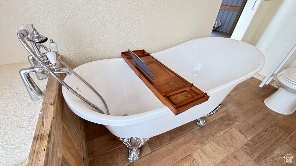 Room details featuring a textured wall, a freestanding tub, and toilet