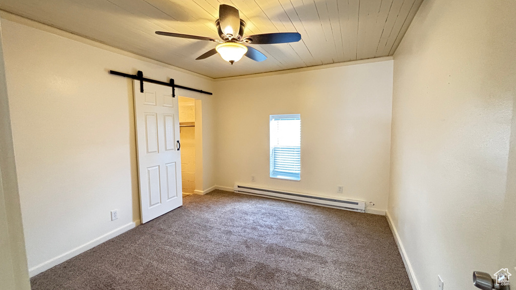 Empty room with carpet flooring, ceiling fan, a barn door, and a baseboard radiator