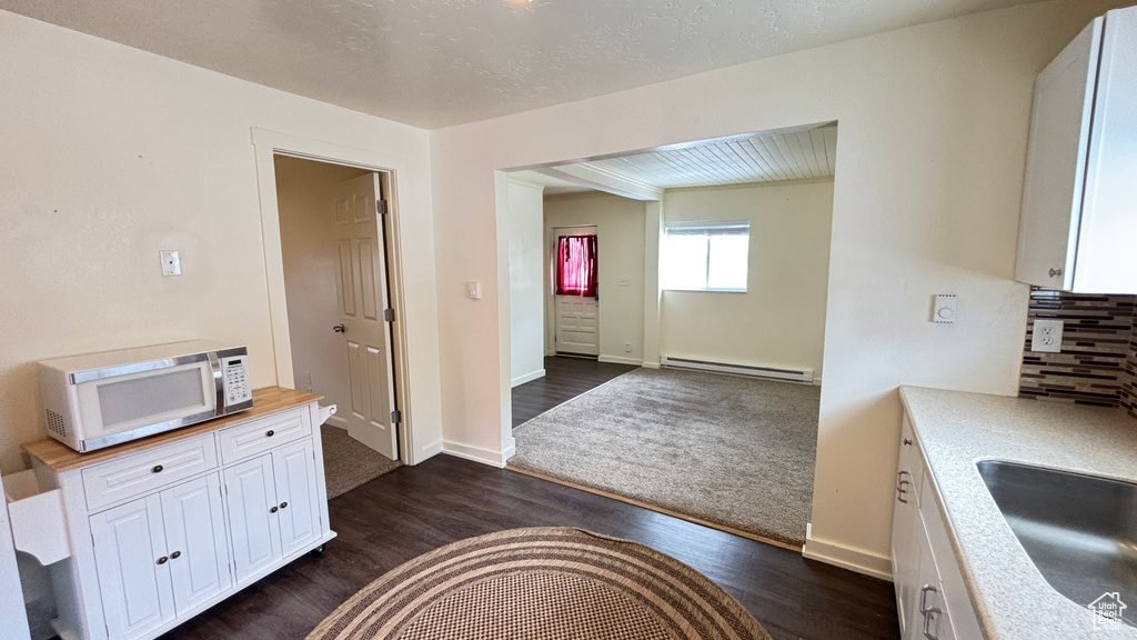 Kitchen featuring a sink, backsplash, baseboard heating, white cabinets, and white microwave