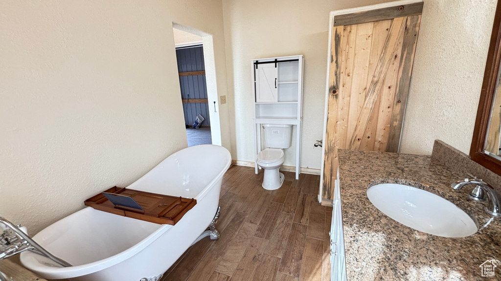 Full bath featuring wood finished floors, a freestanding tub, vanity, and a textured wall