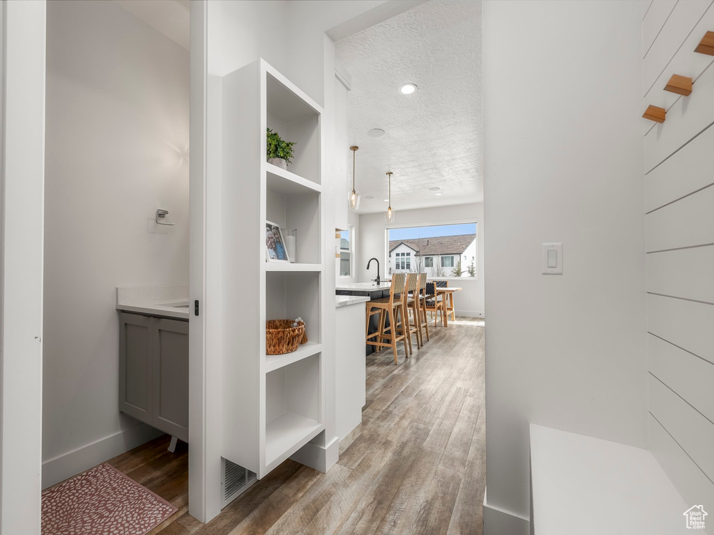 Hall featuring baseboards, wood finished floors, a sink, and a textured ceiling