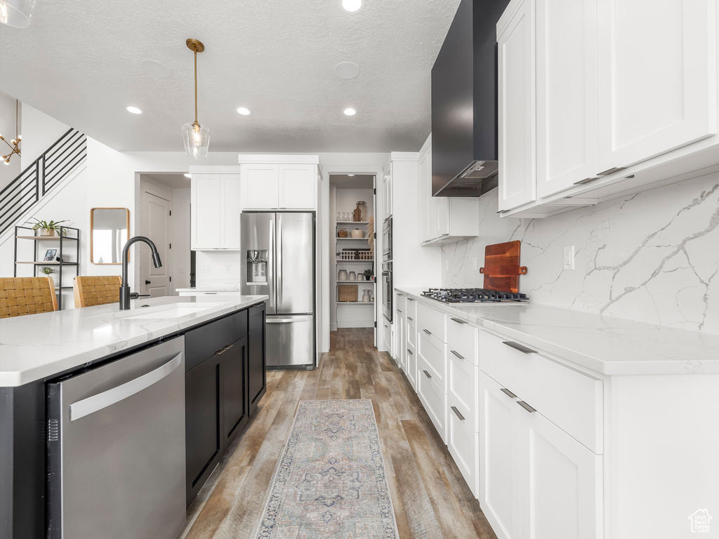 Kitchen with light wood-type flooring, stainless steel appliances, a sink, white cabinets, and wall chimney exhaust hood