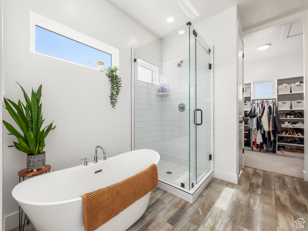 Full bathroom featuring a spacious closet, wood finished floors, a soaking tub, and a shower stall