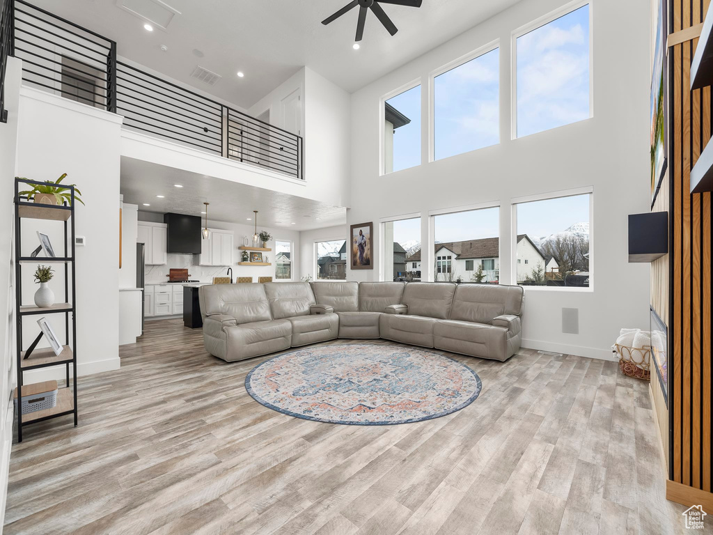 Living room with a high ceiling, baseboards, visible vents, light wood-style floors, and ceiling fan