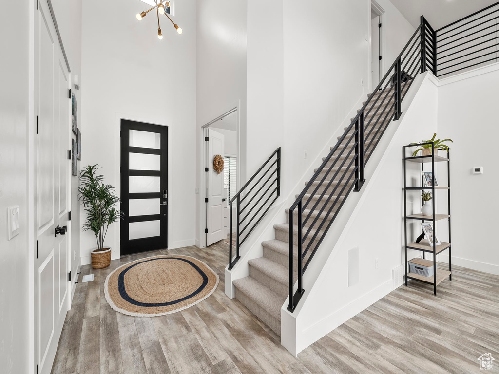 Foyer entrance with stairs, baseboards, a chandelier, a high ceiling, and light wood-style flooring