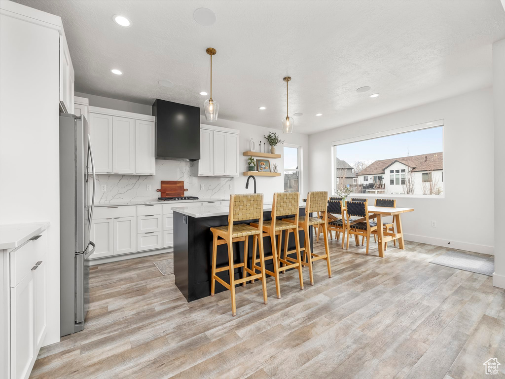 Kitchen featuring backsplash, range hood, a breakfast bar, appliances with stainless steel finishes, and light wood-style flooring