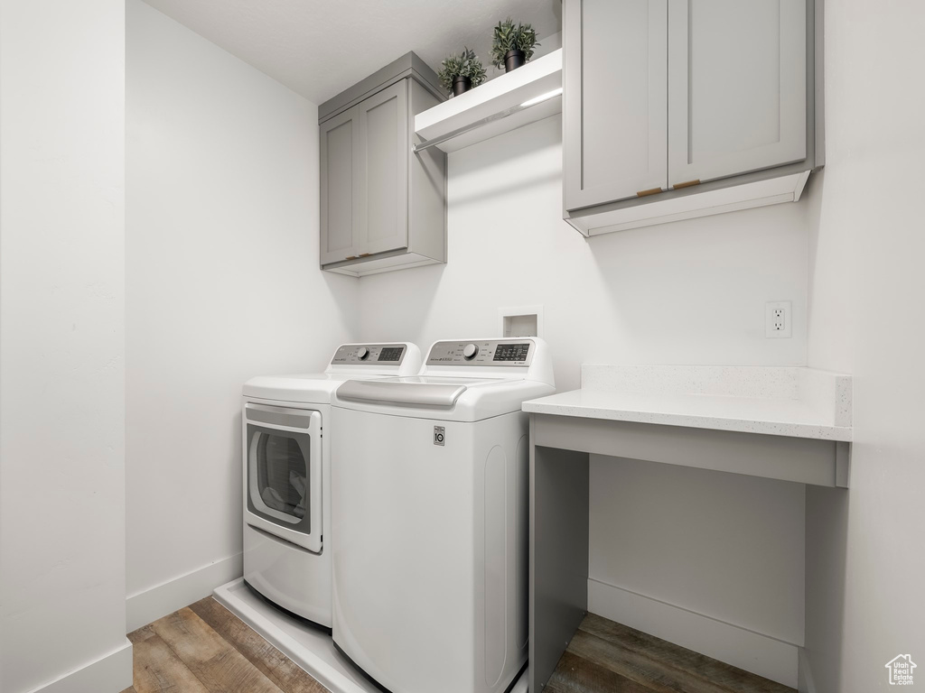Clothes washing area featuring cabinet space, baseboards, washer and dryer, and wood finished floors