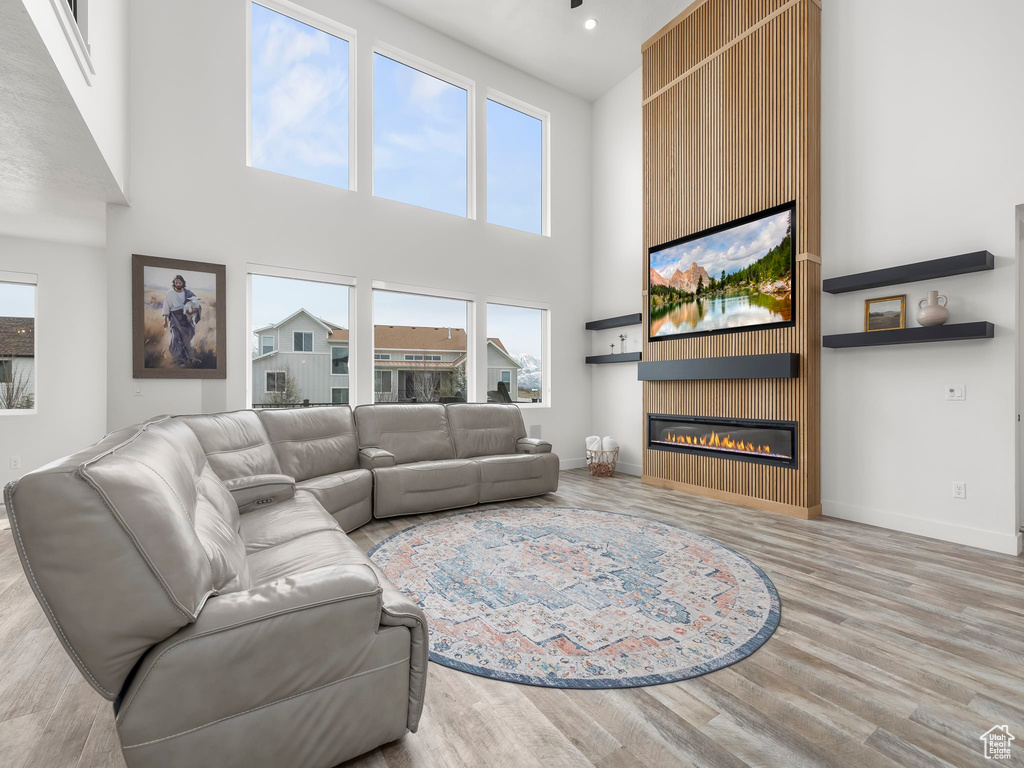 Living room featuring recessed lighting, baseboards, a large fireplace, a towering ceiling, and wood finished floors