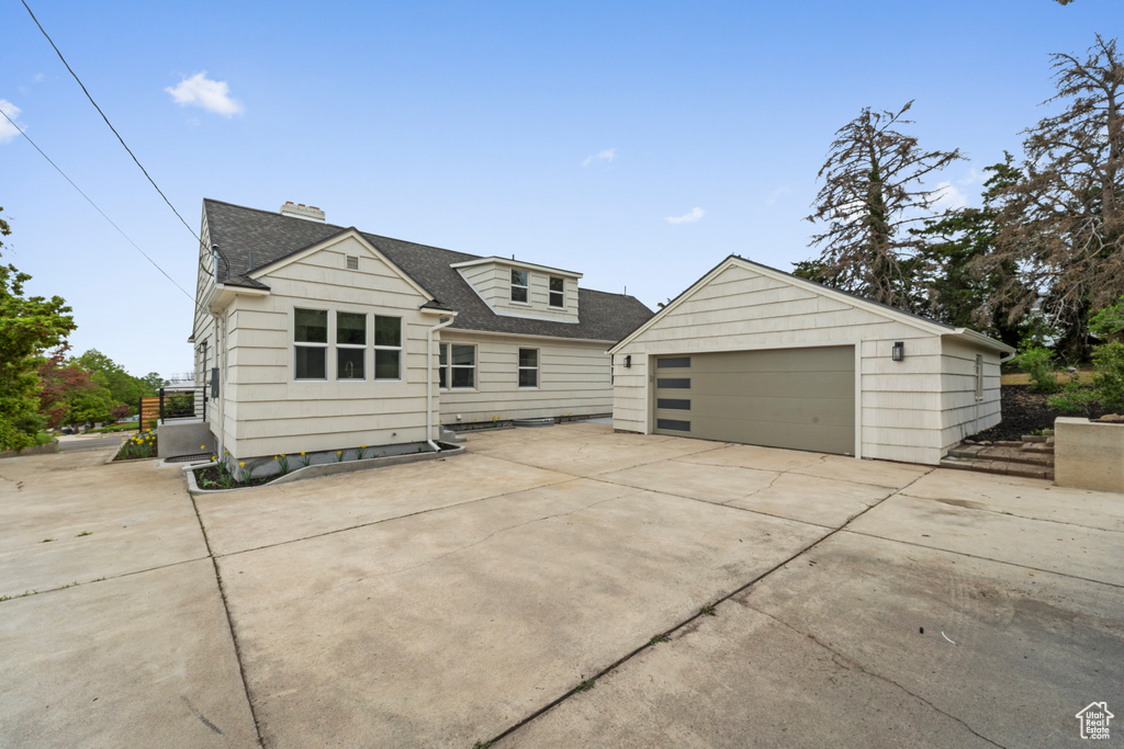 View of front of property with roof with shingles, a garage, a chimney, and an outbuilding