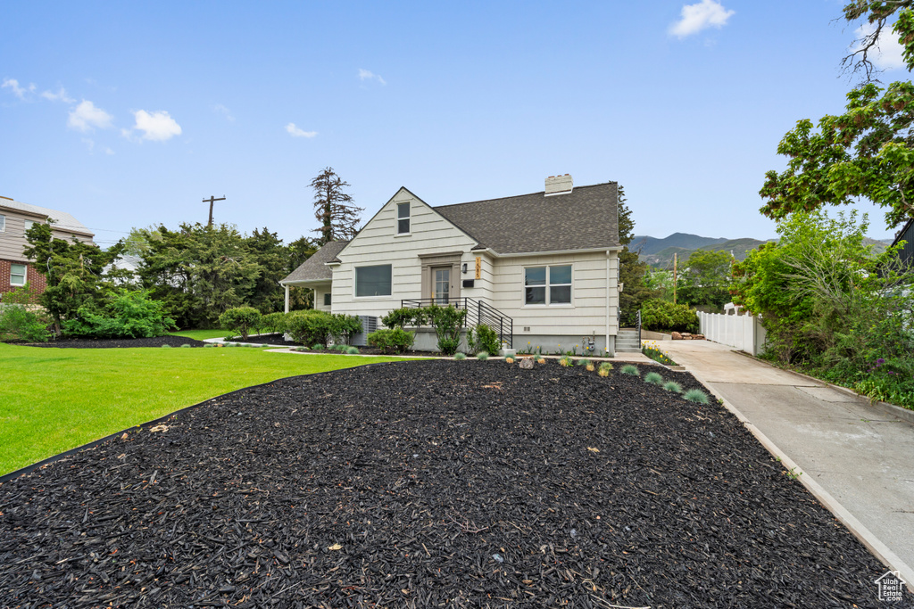 Bungalow with a chimney, driveway, fence, a shingled roof, and a front lawn
