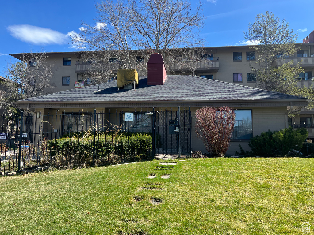 View of front of property with a chimney, a shingled roof, fence, and a front lawn