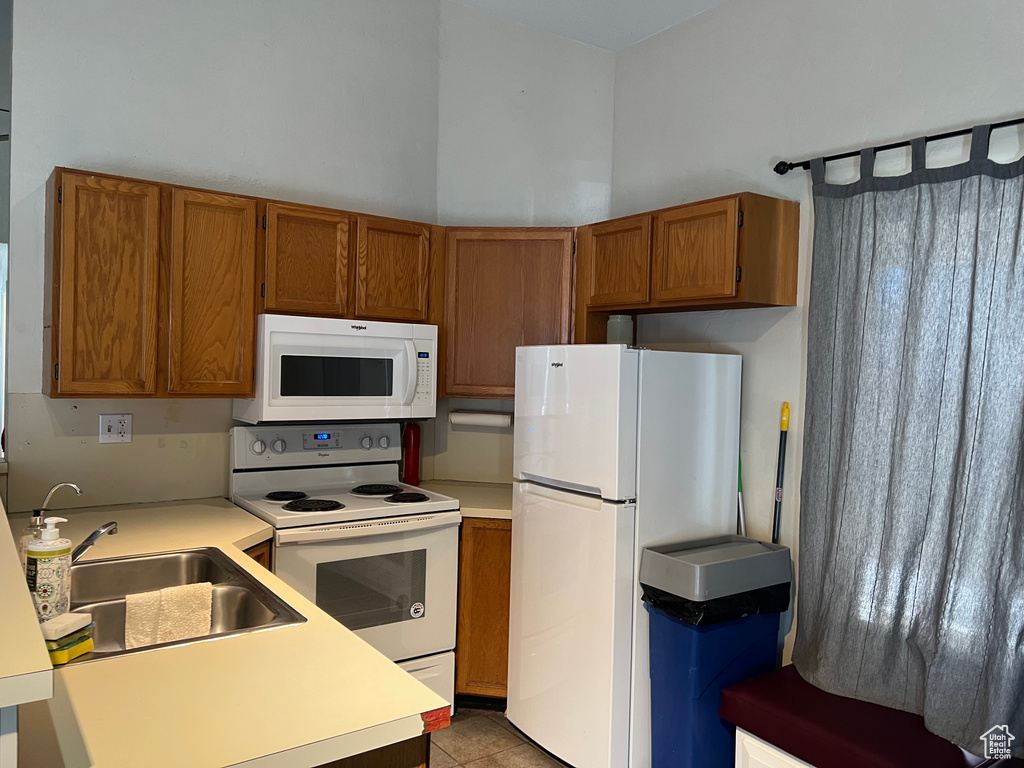 Kitchen with light countertops, white appliances, a high ceiling, a sink, and brown cabinets
