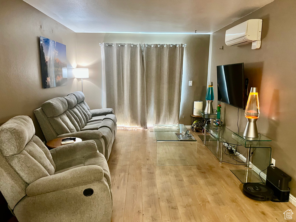 Living area featuring baseboards, light wood-type flooring, and a wall unit AC
