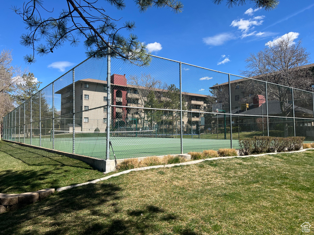 View of sport court featuring fence and a lawn
