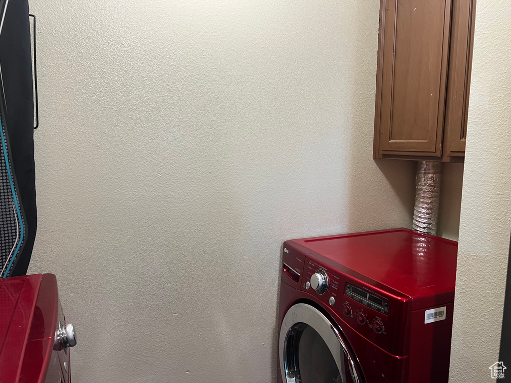 Clothes washing area featuring cabinet space, washer / clothes dryer, and a textured wall