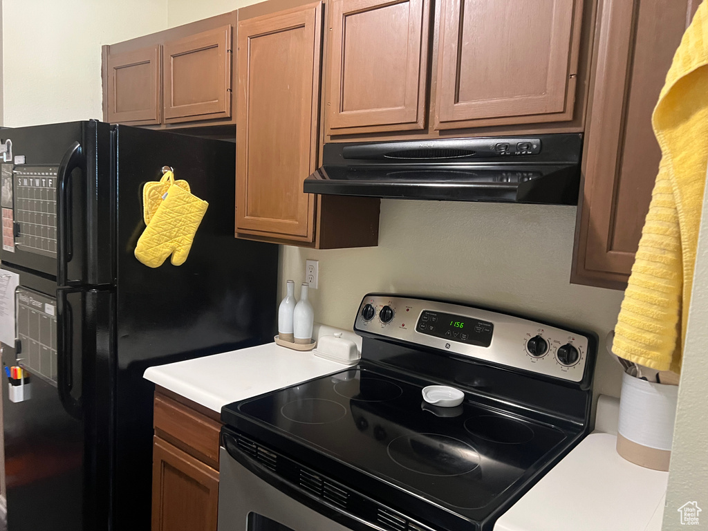 Kitchen featuring freestanding refrigerator, light countertops, under cabinet range hood, and electric stove