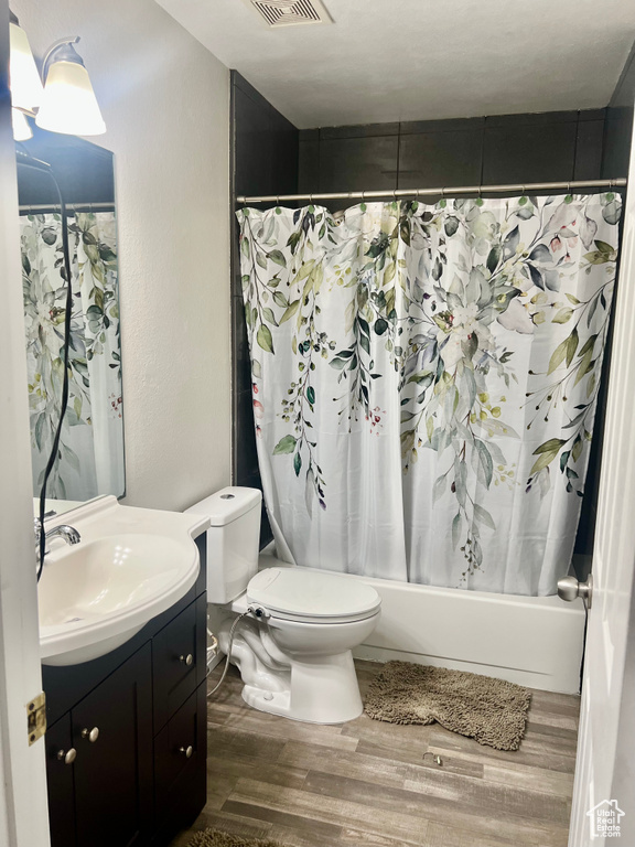 Bathroom with toilet, vanity, shower / bath combo, wood finished floors, and visible vents