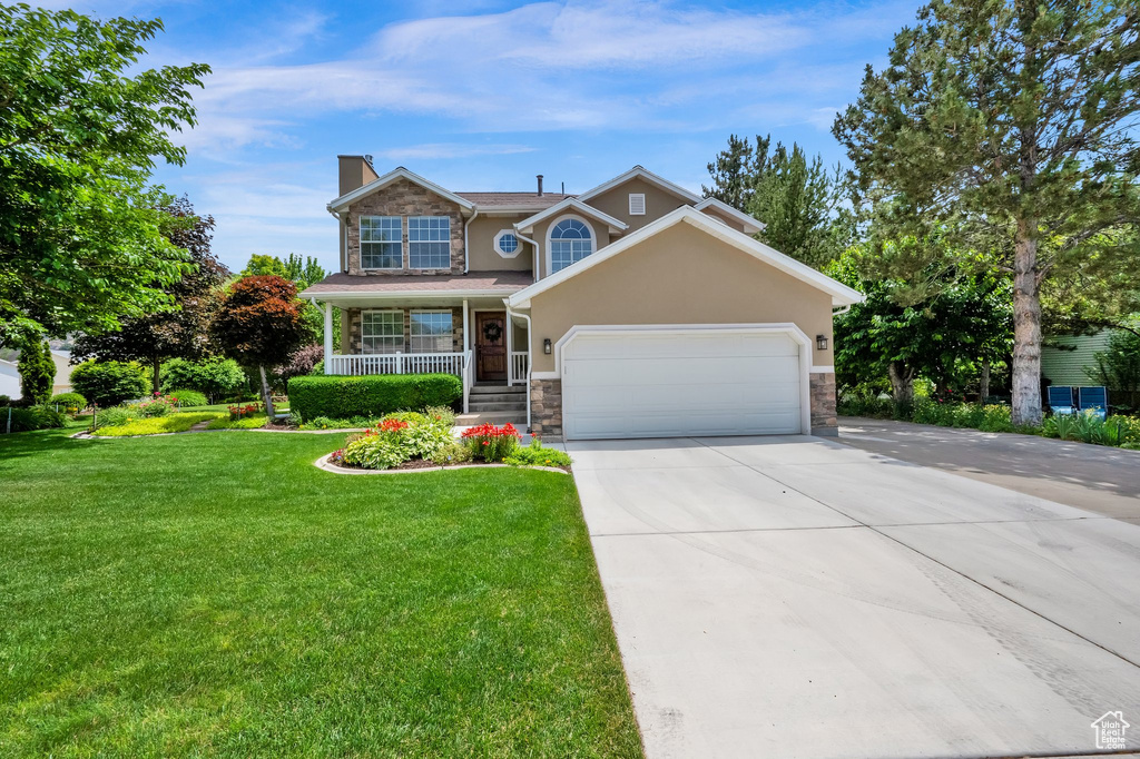 Traditional-style home featuring stone siding, a chimney, an attached garage, concrete driveway, and covered porch