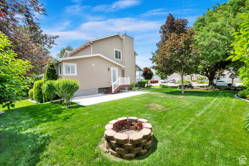View of grassy yard featuring an outdoor fire pit and a patio