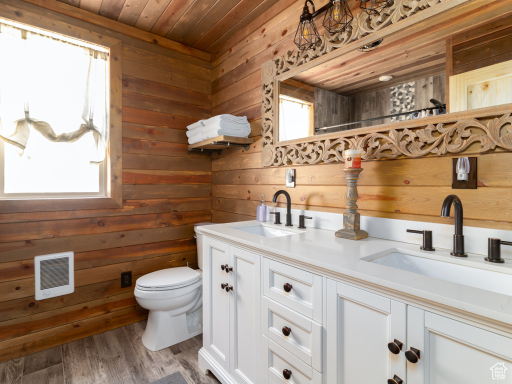Full bathroom with toilet, a sink, wooden walls, visible vents, and double vanity