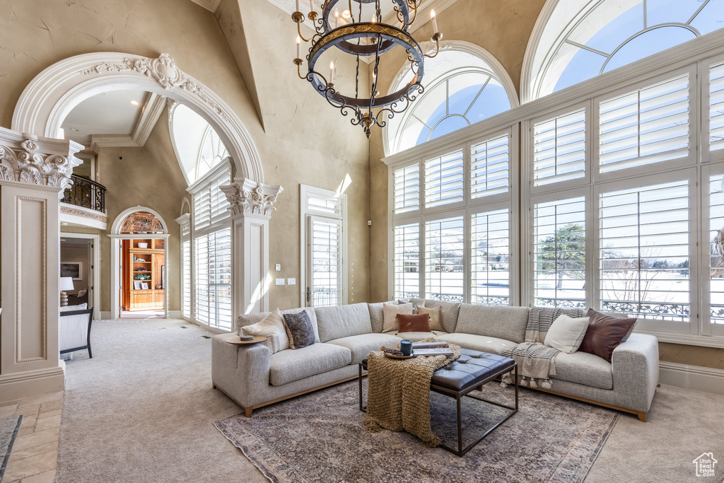 Carpeted living room with baseboards, an inviting chandelier, a towering ceiling, and ornate columns