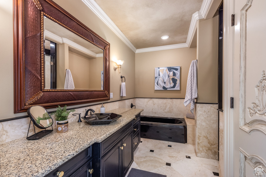 Full bath featuring tile walls, crown molding, vanity, a garden tub, and wainscoting