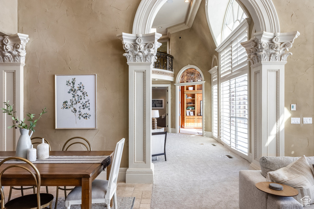 Dining area featuring stone tile flooring, a towering ceiling, light colored carpet, and ornate columns