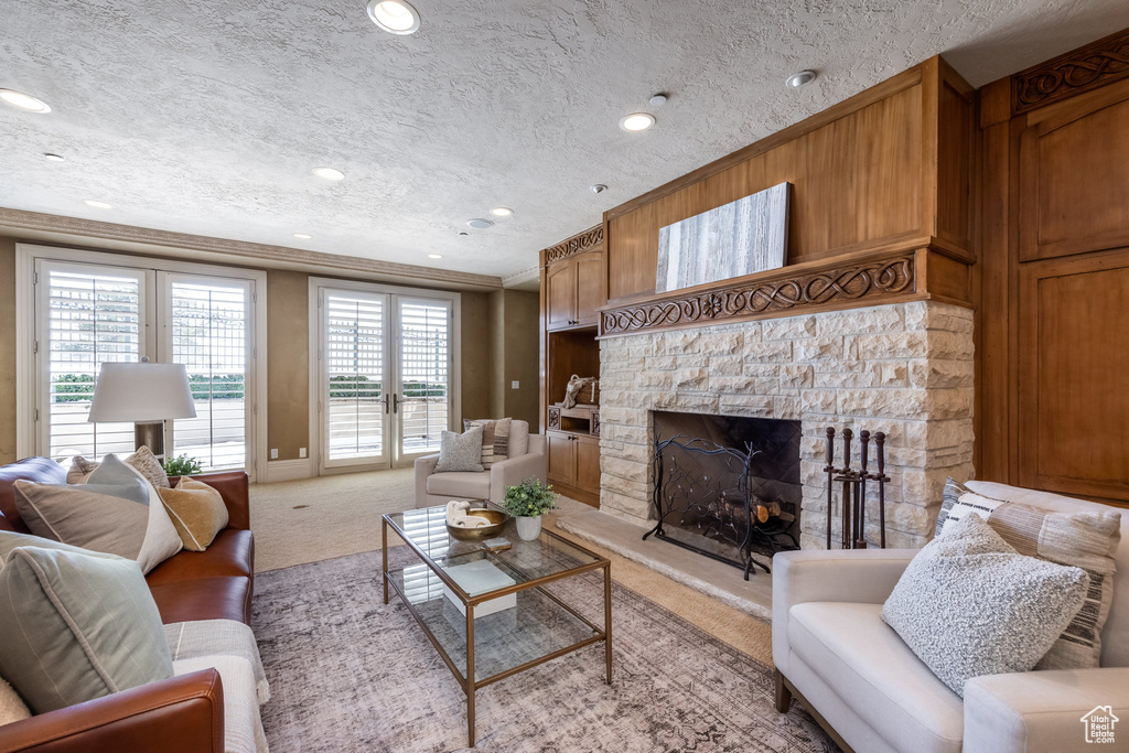 Carpeted living area featuring a textured ceiling, recessed lighting, ornamental molding, and a stone fireplace