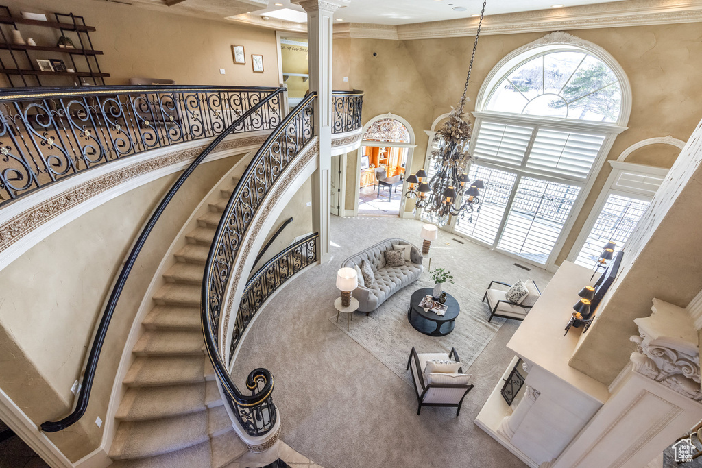 Stairway featuring decorative columns, crown molding, carpet flooring, a towering ceiling, and an inviting chandelier