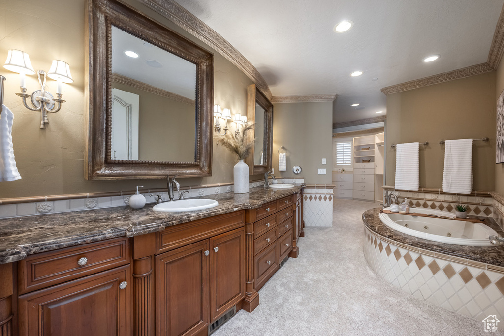 Full bath with double vanity, a sink, a jetted tub, and crown molding