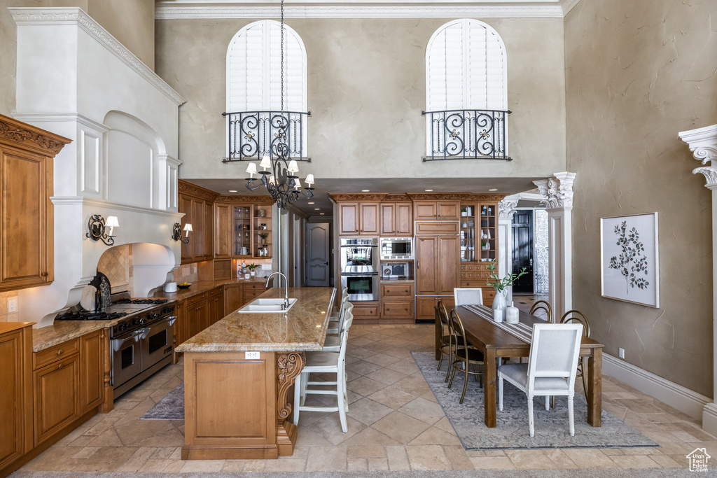 Kitchen featuring a sink, a breakfast bar area, built in appliances, brown cabinetry, and a notable chandelier