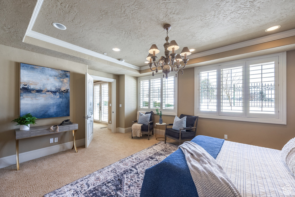 Carpeted bedroom featuring baseboards, ornamental molding, a notable chandelier, and a raised ceiling