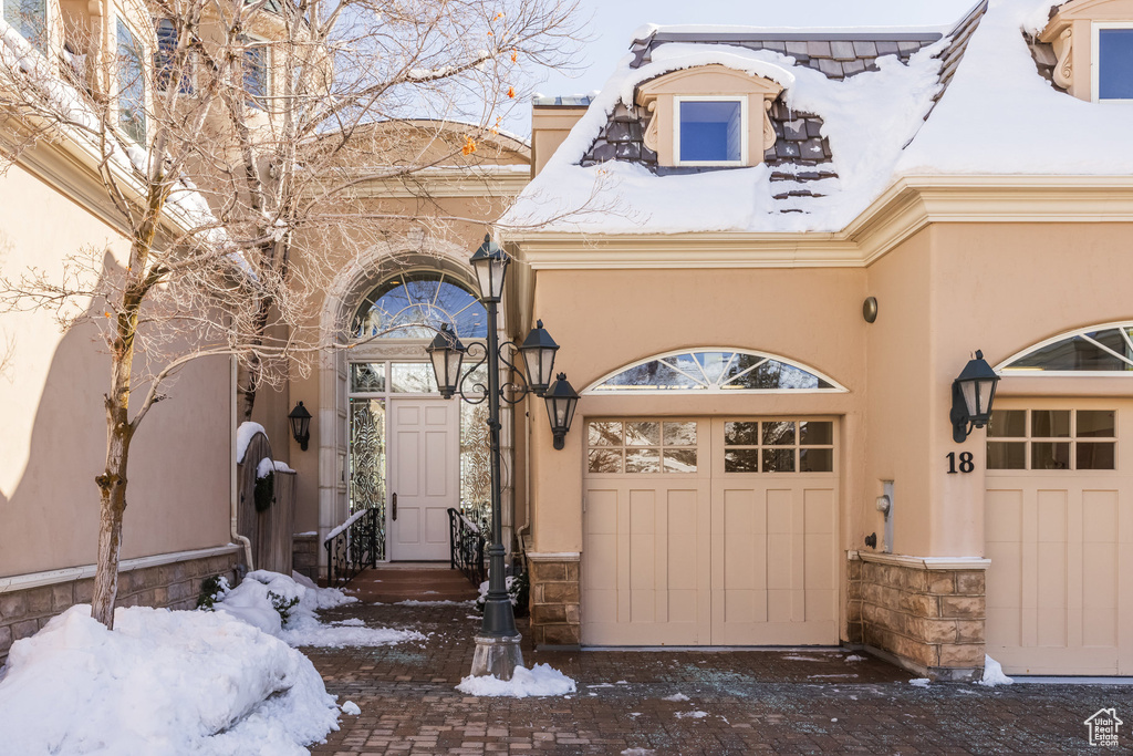 Snow covered property entrance featuring driveway, a garage, and stucco siding