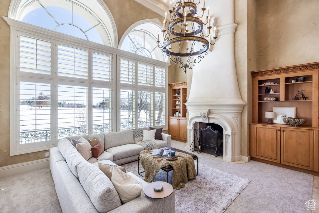 Living area featuring a fireplace with flush hearth, a chandelier, baseboards, a towering ceiling, and light colored carpet
