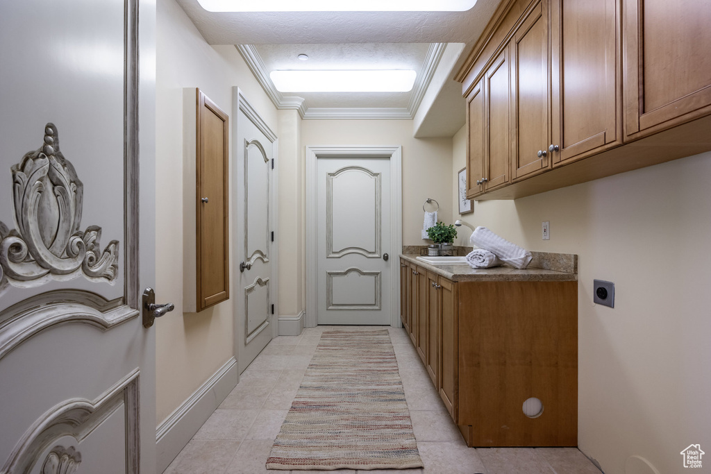 Laundry area with crown molding, light tile patterned floors, baseboards, cabinet space, and electric dryer hookup