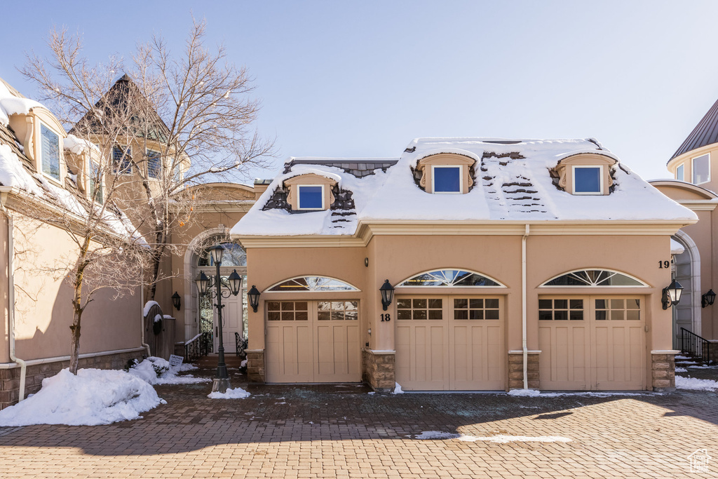 View of front of property featuring driveway, stone siding, a garage, and stucco siding