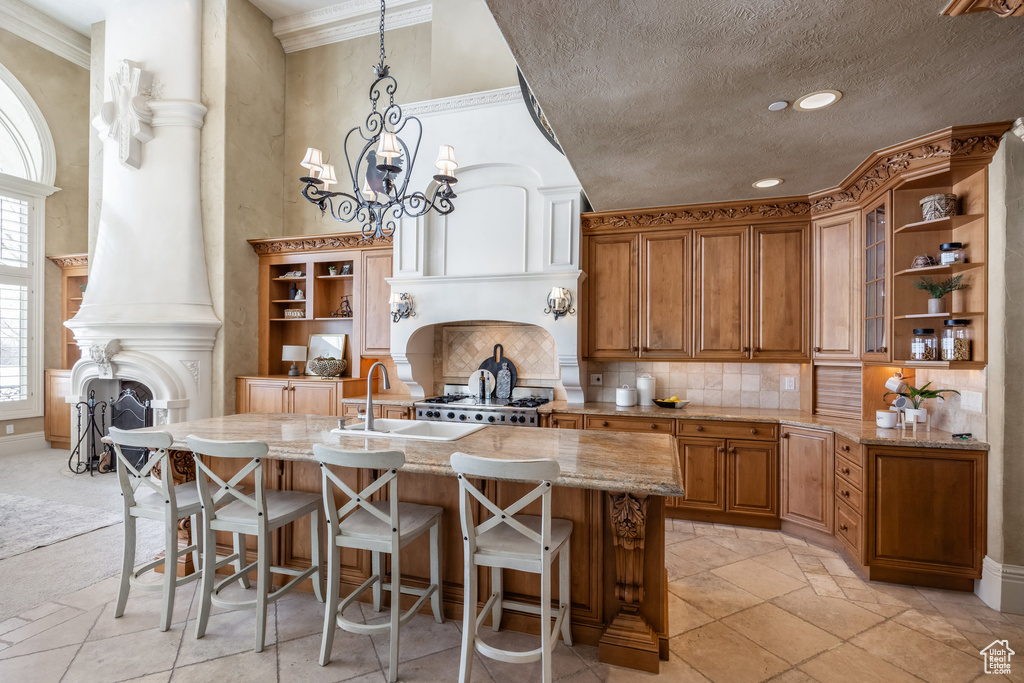 Kitchen with open shelves, decorative backsplash, a sink, light stone counters, and brown cabinets