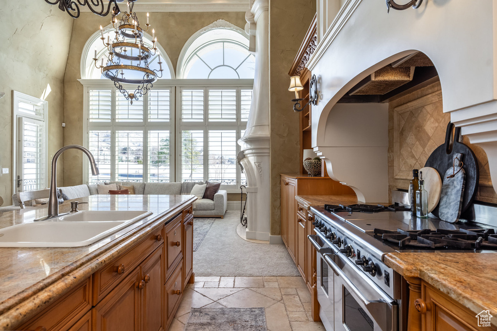 Kitchen featuring a sink, double oven range, a high ceiling, brown cabinets, and stone tile flooring