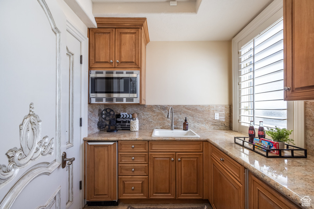 Kitchen featuring a sink, decorative backsplash, stainless steel microwave, and brown cabinets