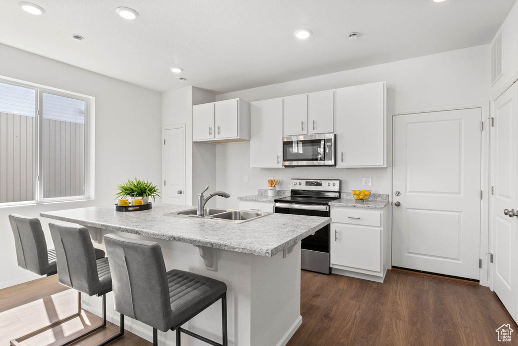 Kitchen featuring dark wood-style flooring, light countertops, stainless steel appliances, white cabinetry, and a sink