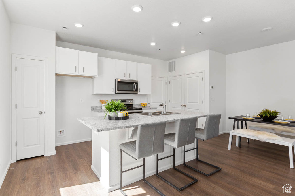 Kitchen with dark wood finished floors, a center island with sink, appliances with stainless steel finishes, white cabinetry, and a sink