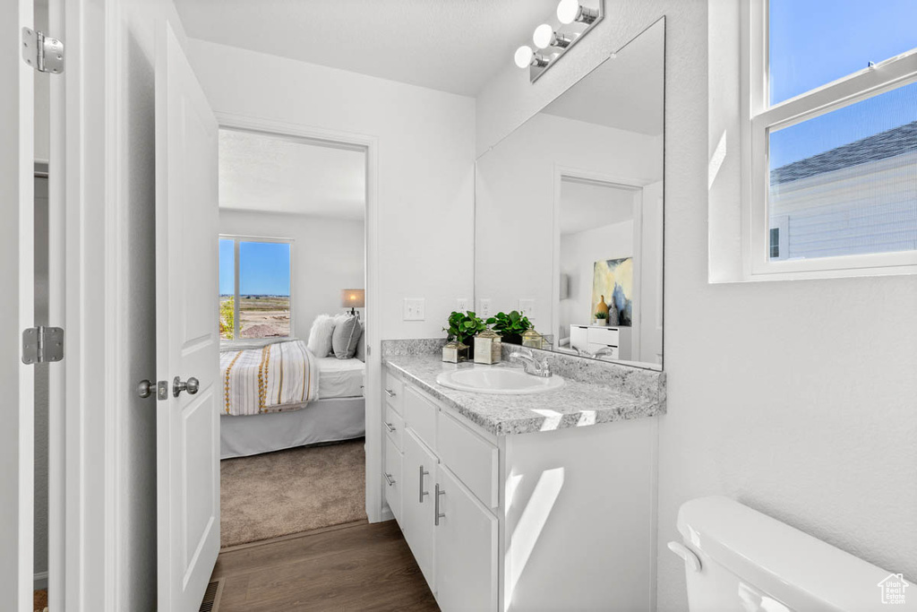 Ensuite bathroom with toilet, vanity, ensuite bath, and wood finished floors