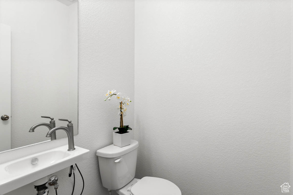 Half bathroom with a textured wall, a sink, and toilet