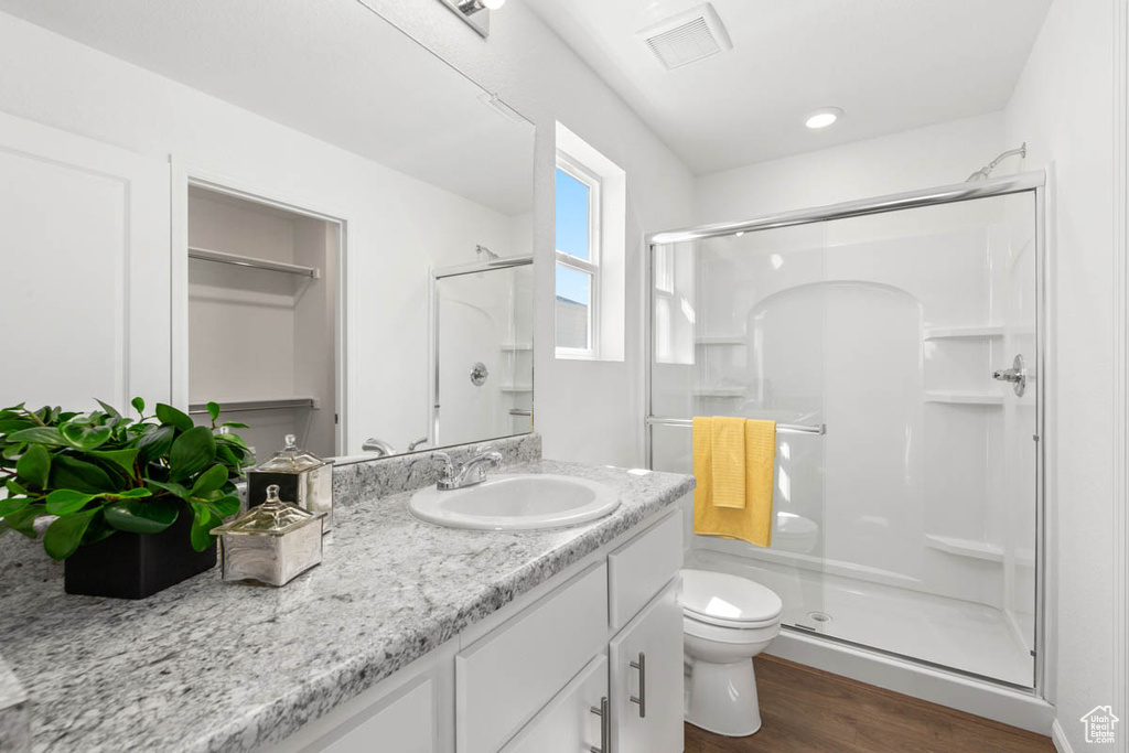 Bathroom featuring toilet, vanity, a shower stall, wood finished floors, and visible vents