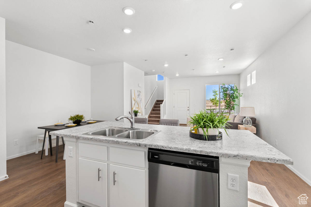 Kitchen featuring dishwasher, wood finished floors, an island with sink, a sink, and open floor plan